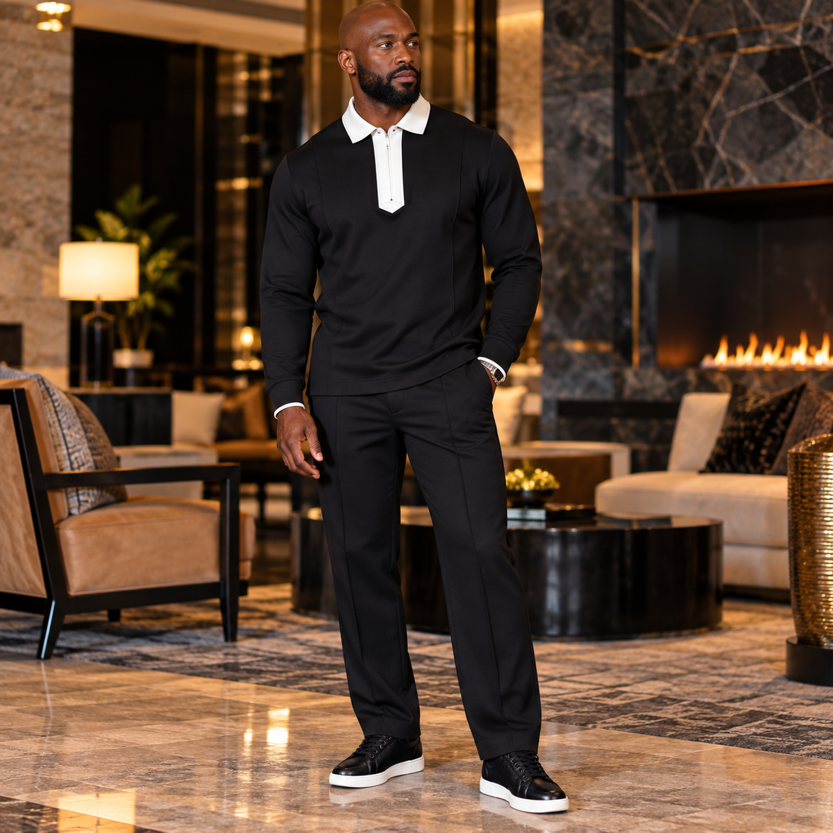A man wearing a Suit Yourself Menswear black two-piece set with a white contrast quarter-zip collar in a luxury lounge.