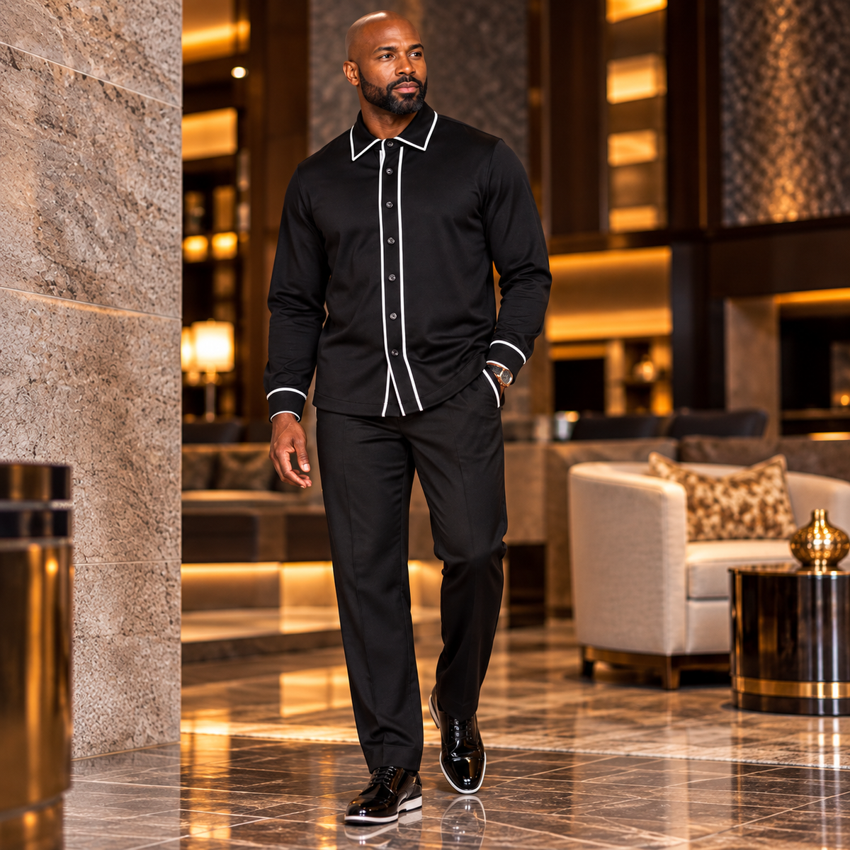 A man wearing a black two-piece casual set by suit-yourself-menswear with white contrast piping in a luxury hotel.